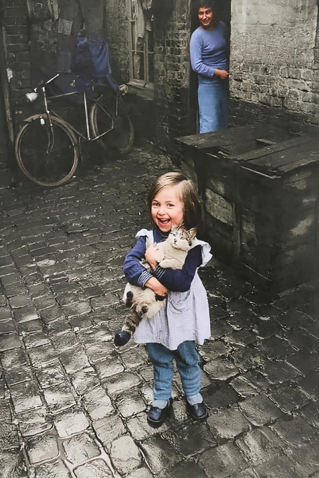 Restored photo of girl with cat in cobblestone alley